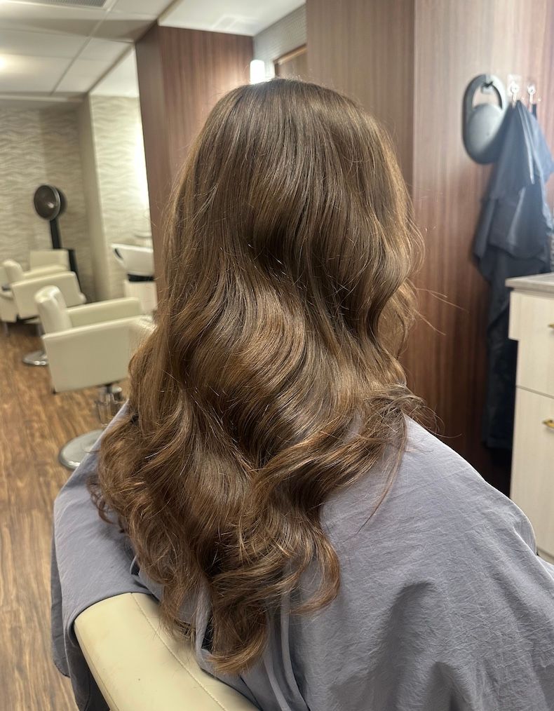 Long brunette in soft glossy waves, seen from behind in the salon chair